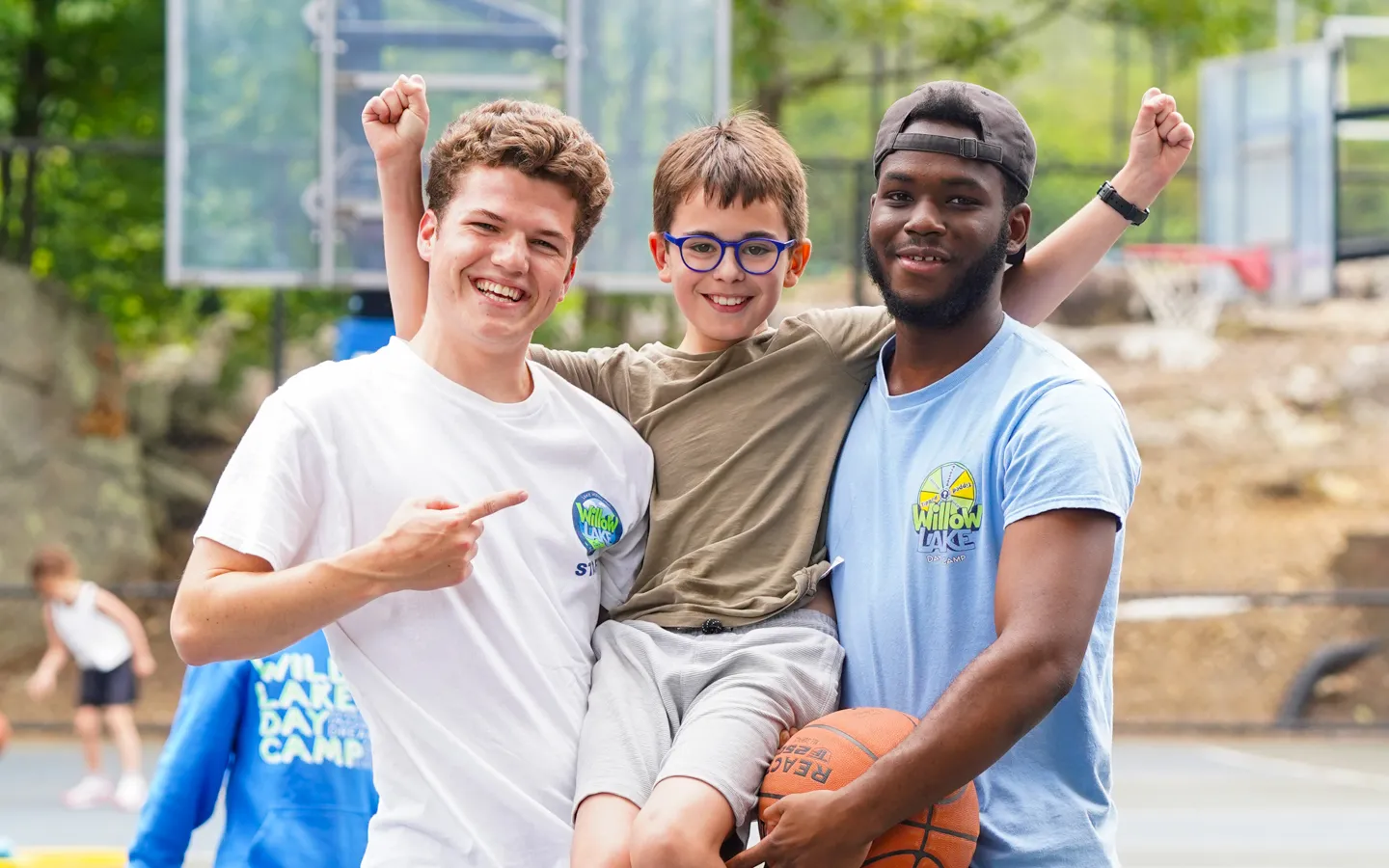 Two Willow Lake specialists celebrating with a camper on the basketball courts