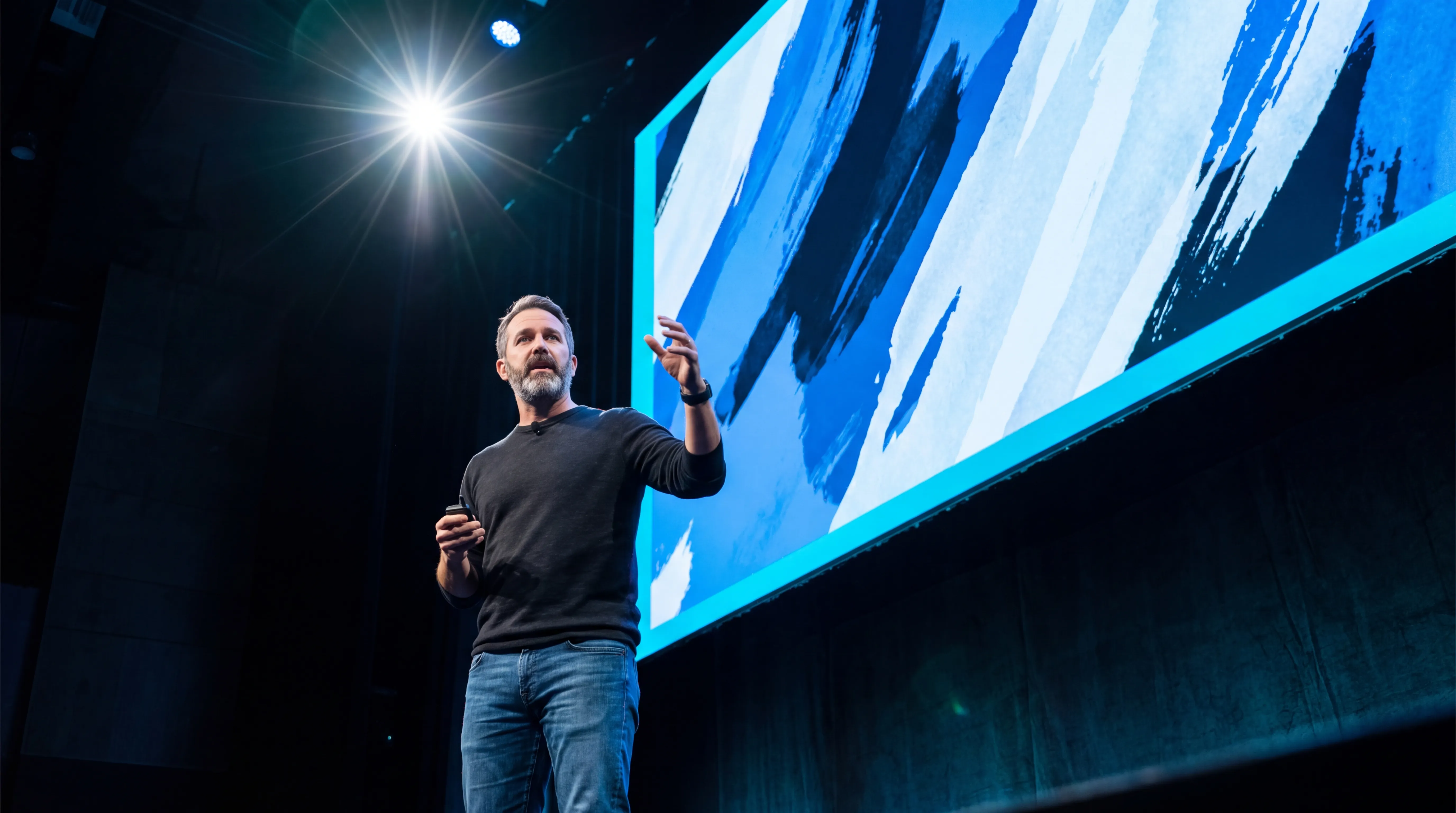 Speaker presenting on stage beside a large blue screen