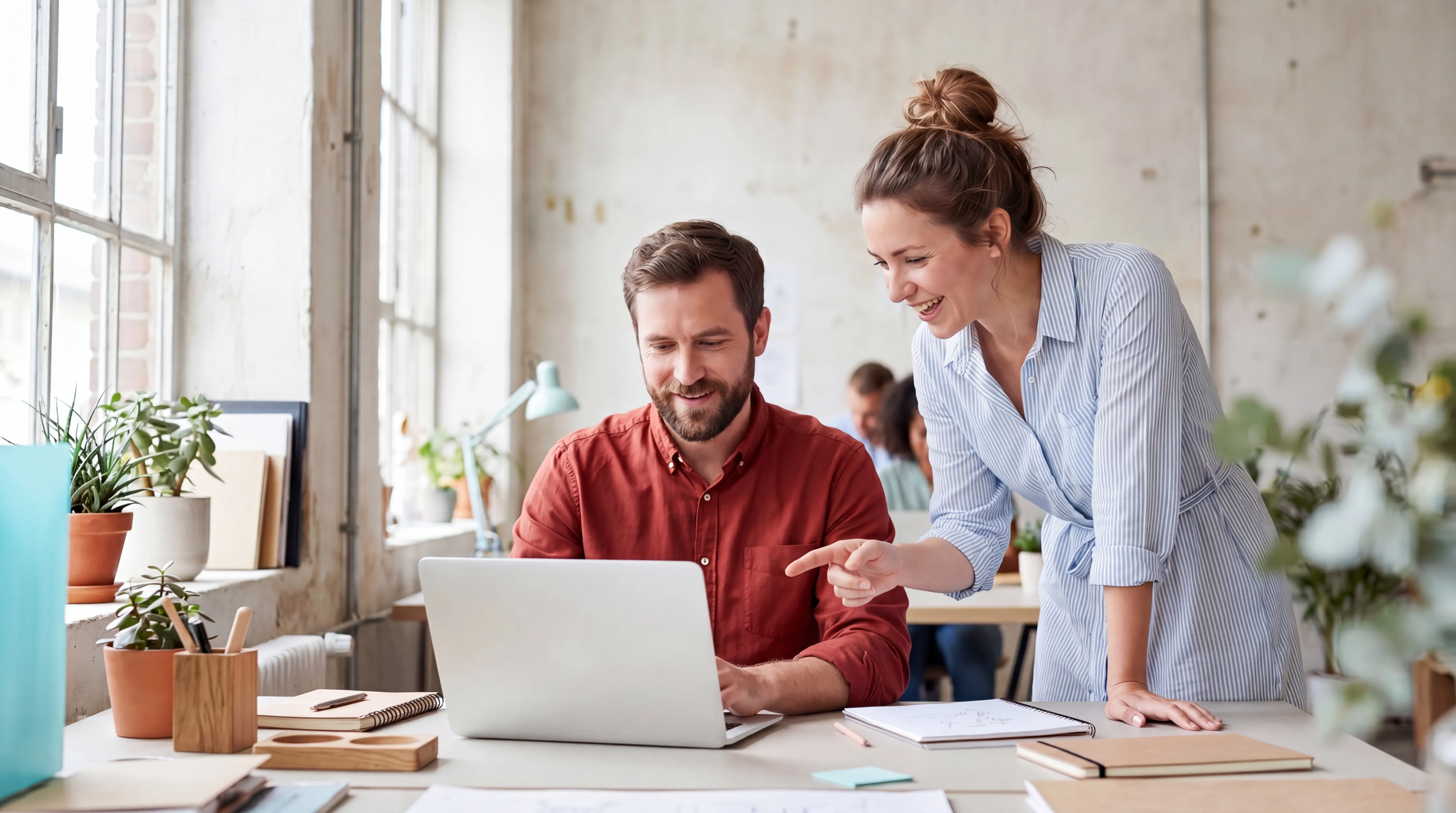 Two people smiling while collaborating on a laptop in an office